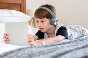 Ein Junge liegt auf dem Bett und schaut ein Video auf seinem iPad.