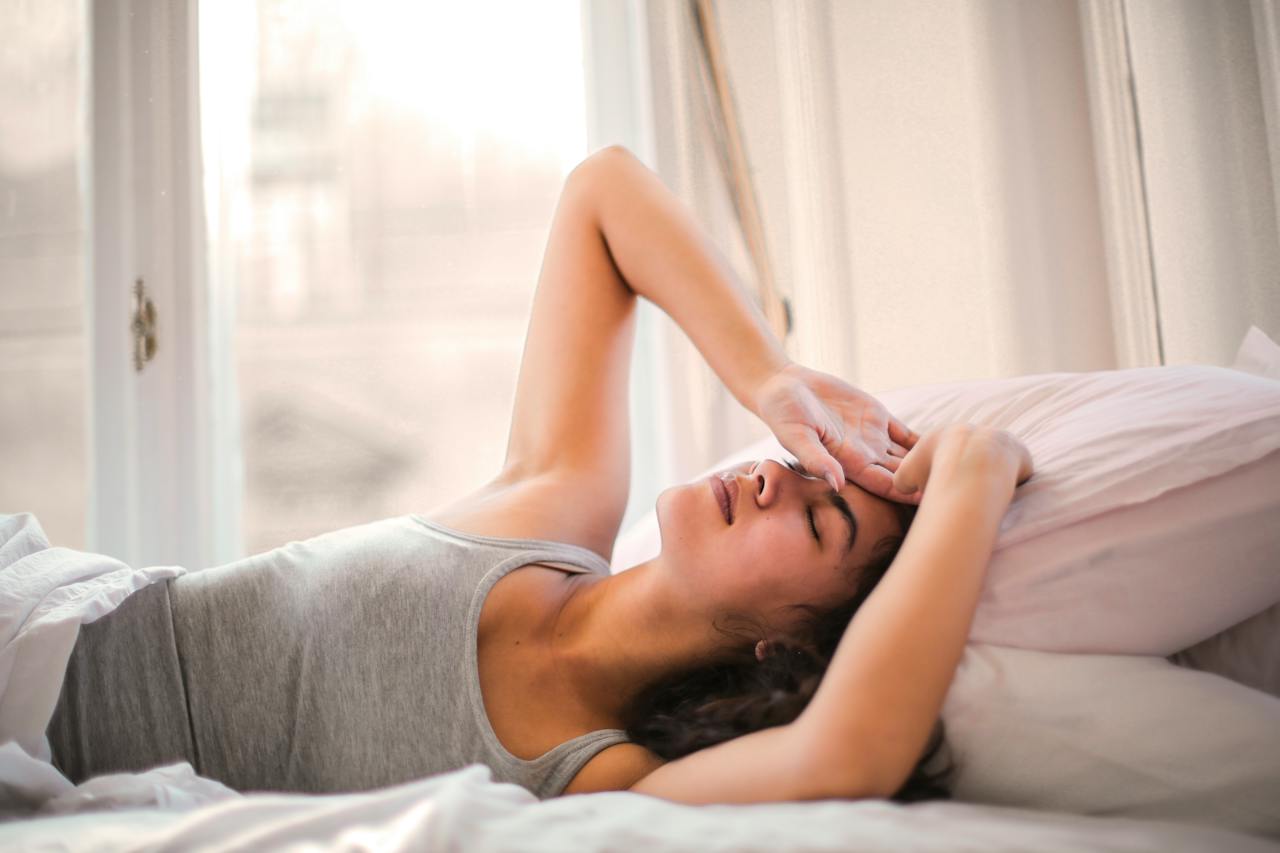 Eine Frau liegt mit Kopfschmerzen im Bett.