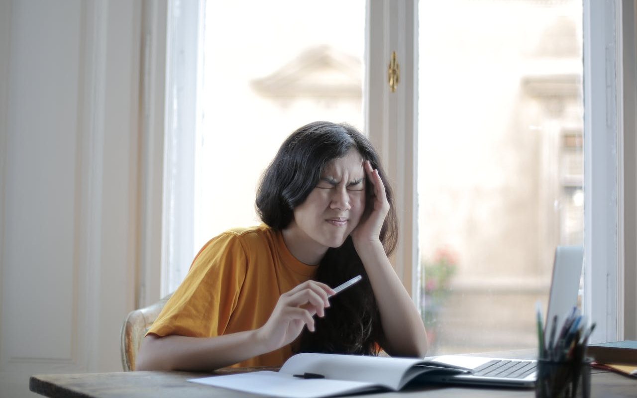 Eine Frau sitzt am Schreibtisch und hält sich vor Schmerz den Kopf