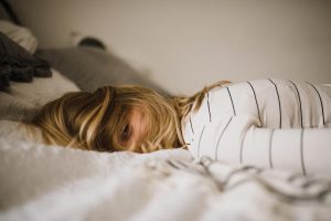 Eine Frau liegt erschöpft und antriebslos auf ihrem Bett.