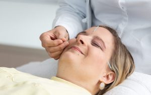 Eine Frau liegt auf einer Liege mit AKupunkturnadeln im Gesicht.