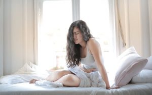 Eine Frau sitzt im Bett und hält Schmerzverzerrt ihren Bauch