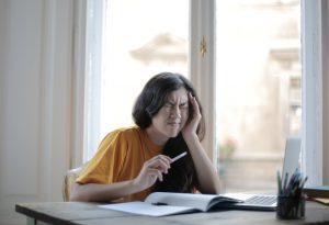 Eine Frau sitzt am Schreibtisch und hält sich vor Schmerz den Kopf